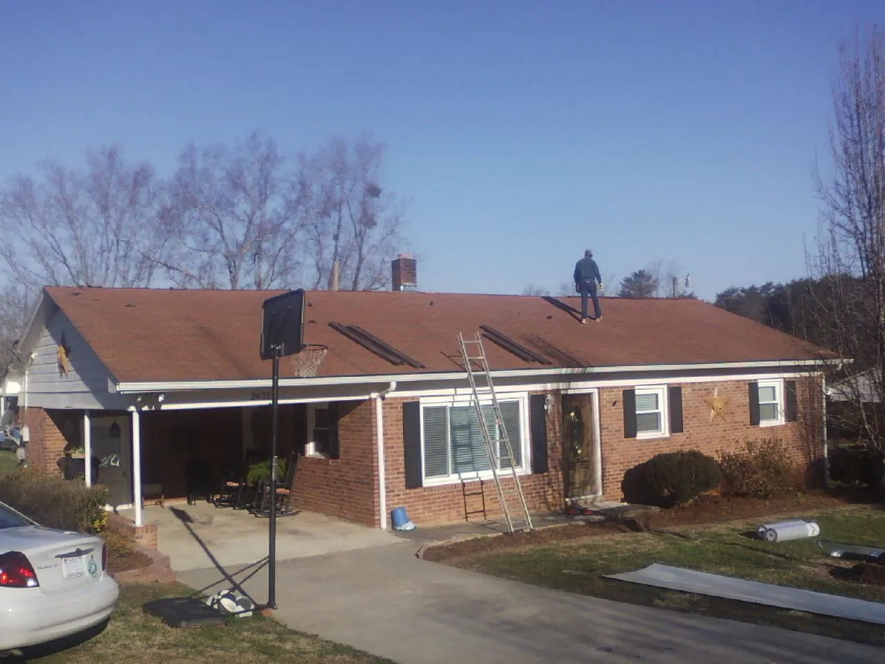 Roofer stripping a shingle roof on a brick ranch before metal panels in Pleasant Lake