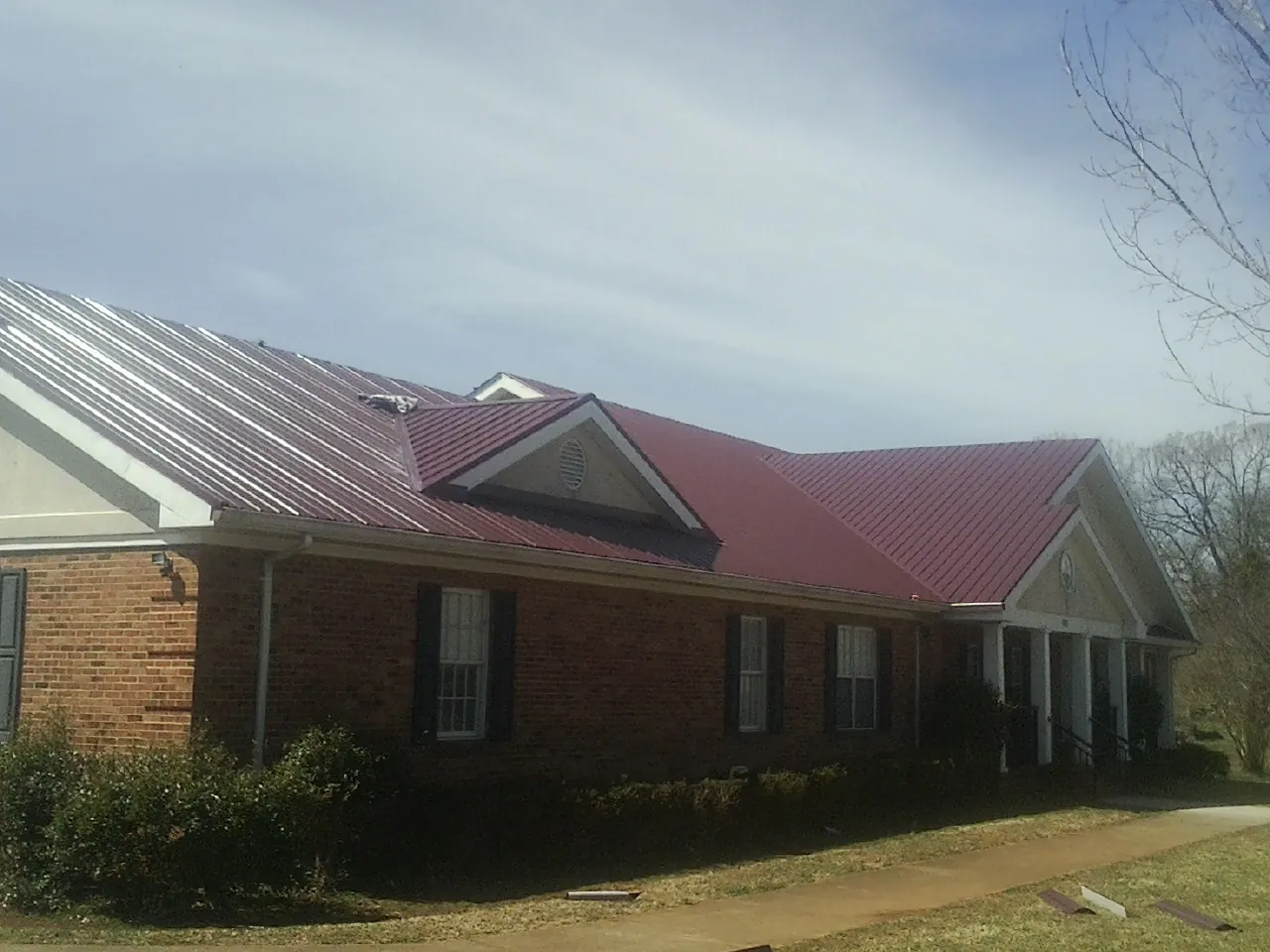 Red metal roof with gabled entries on a long brick building, from a Hail Damage Roof Repair job in Pleasant Lake