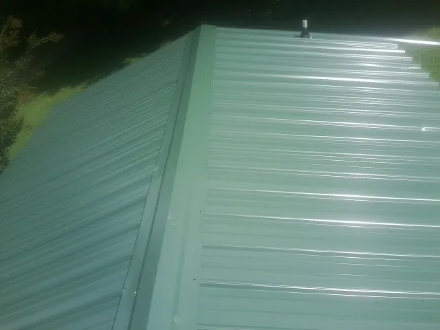 New green metal panels meeting at the ridge of a roof — Flat Roof Repair work by our crew in Pleasant Lake