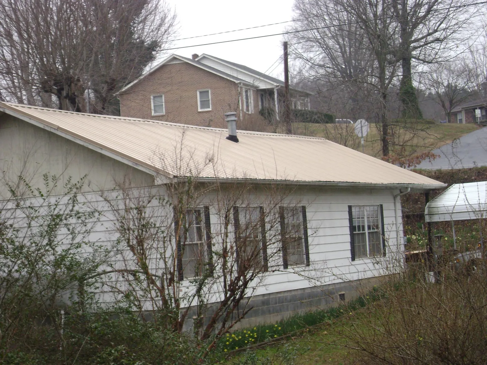 Tan metal roof on a white sided house set into a hillside — Commercial Roofing by Roofing Brothers in Pleasant Lake