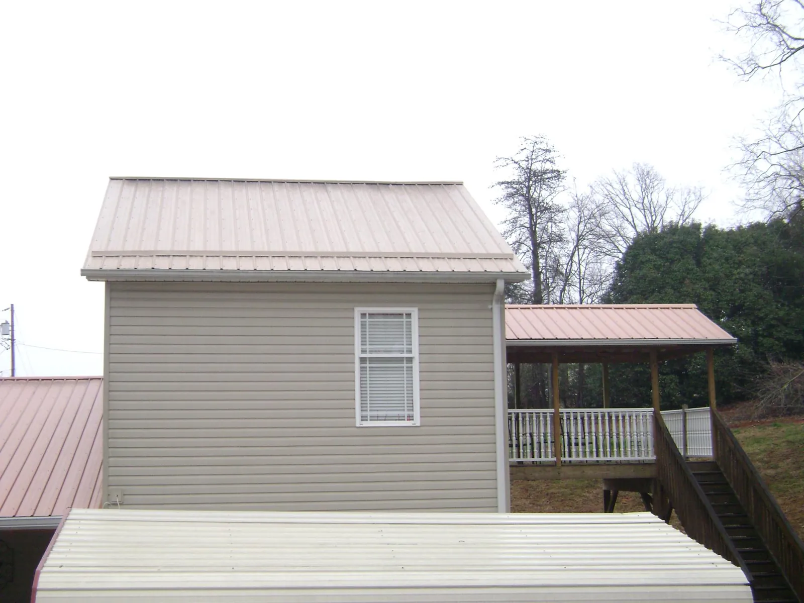 Tan metal roofs on a two story addition and attached porch, from a Roof Replacement job in Pleasant Lake