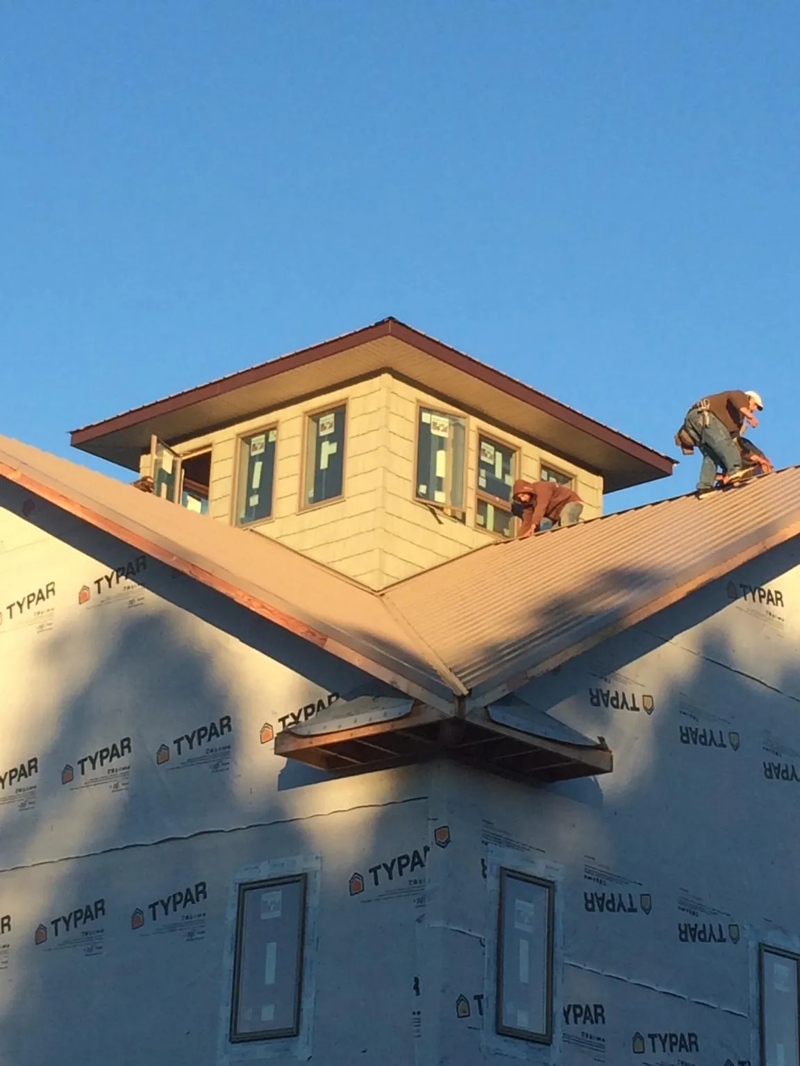 Roofers working around a rooftop cupola on a new metal roof at sunset — Roof Waterproofing in Pleasant Lake by Roofing Brothers